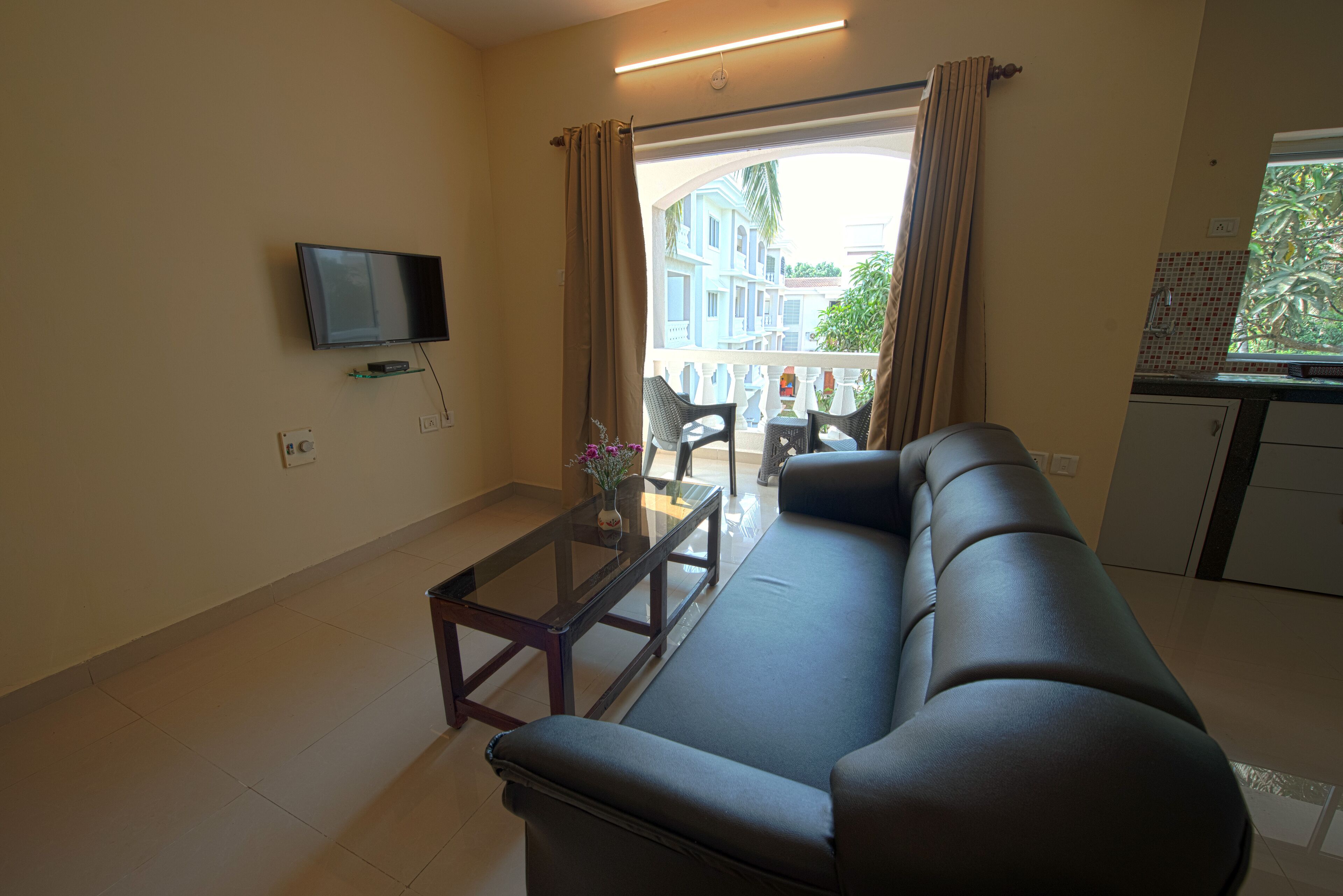 Een woonkamer met een bank, een glazen salontafel, een flatscreen televisie aan de muur en uitzicht op het balkon.