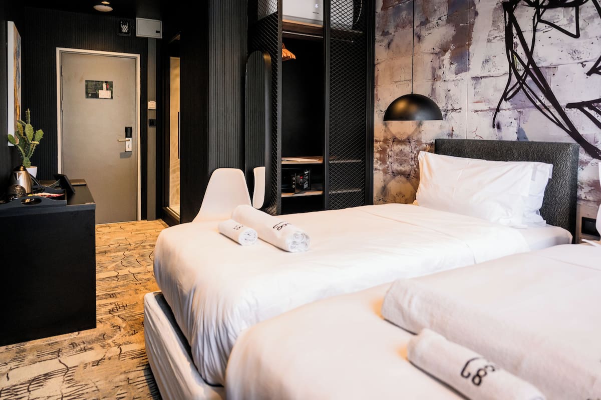 A hotel room with a bed, a desk, a chair, a wardrobe, and a wall with abstract art.