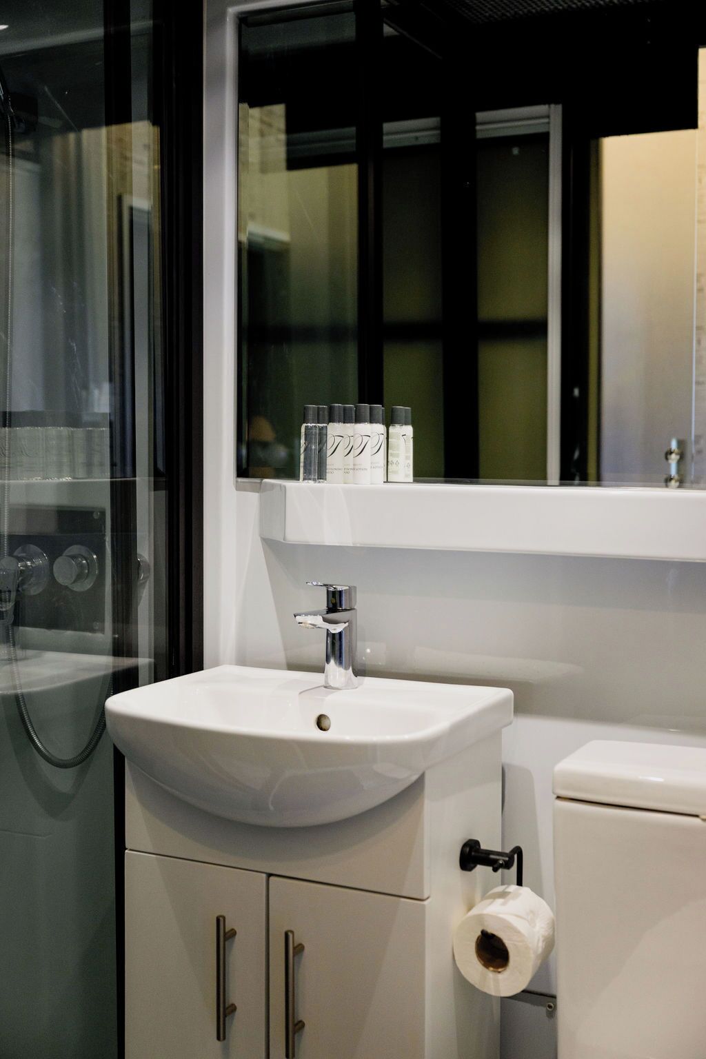 A modern bathroom with a white sink, a toilet, and a glass shower enclosure.