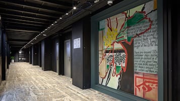 A hallway with a patterned floor, a large abstract mural on the wall, and a sign indicating room numbers.