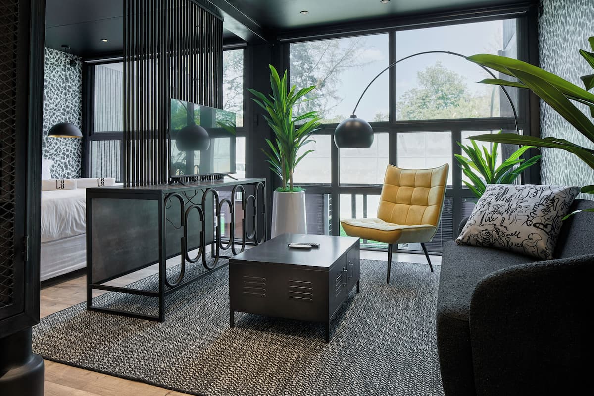 A modern living room with a sofa, a yellow chair, a coffee table, and a large window with a view of trees.