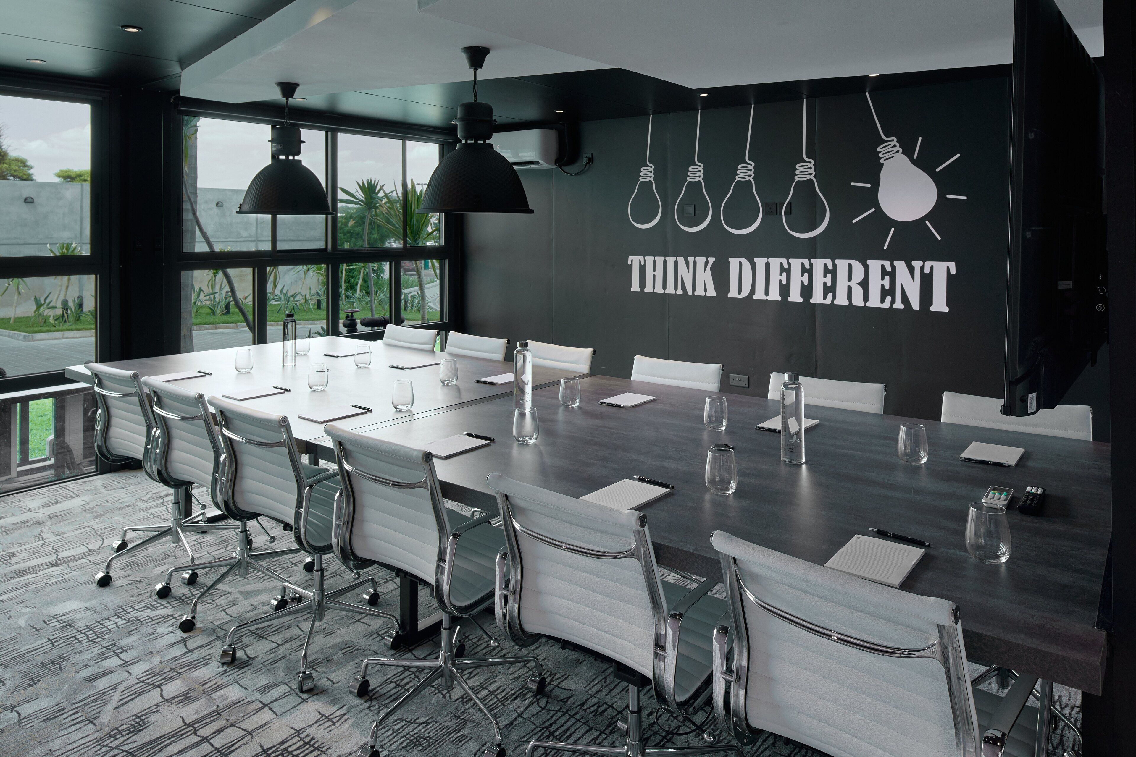 Et mødelokale med et langt bord, hvide stole og en motiverende væg med teksten "THINK DIFFERENT".