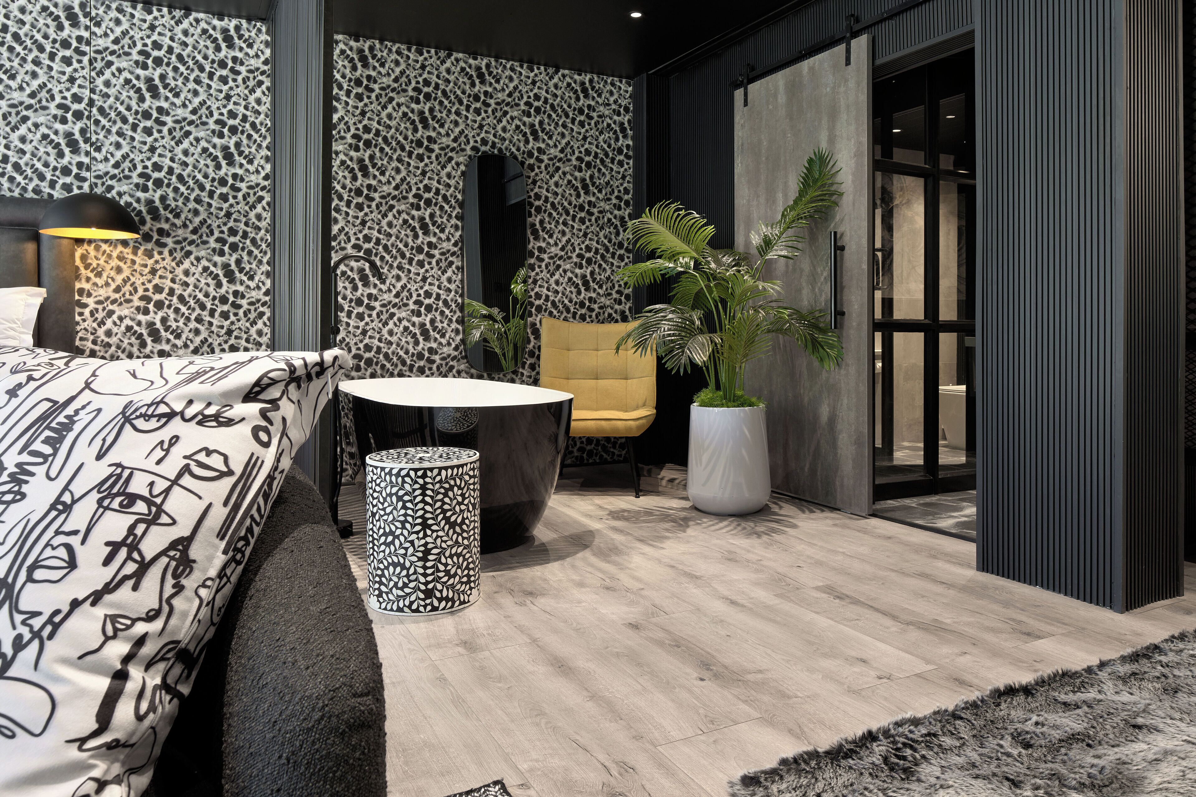 A modern bedroom with a bed, a round table, a chair, and a potted plant.