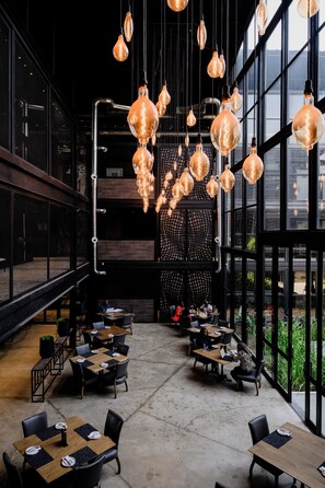 Um interior moderno com luminárias pendentes, mesas, cadeiras e amplas janelas.