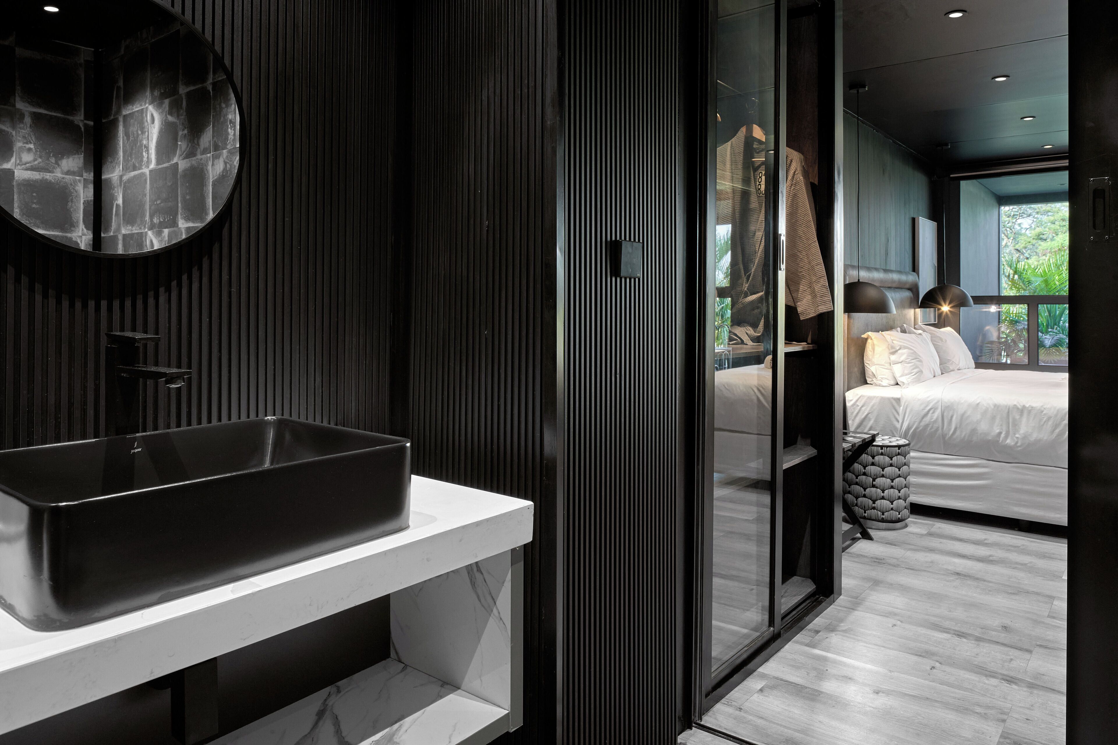A modern bathroom with a large rectangular sink, a round mirror, and a dark wooden panel wall.