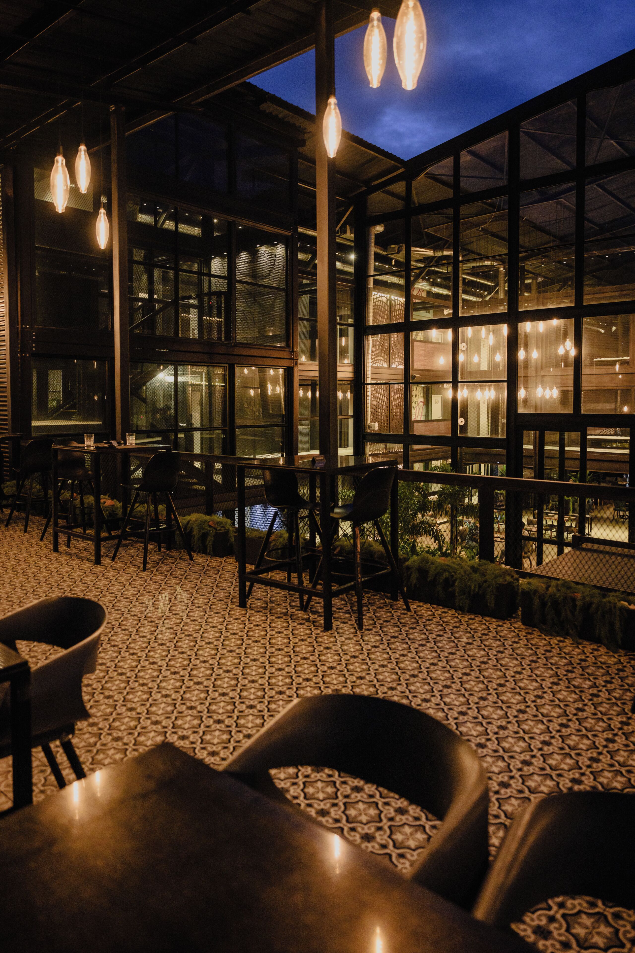 A restaurant with a tiled floor, tables, chairs, and hanging lights.