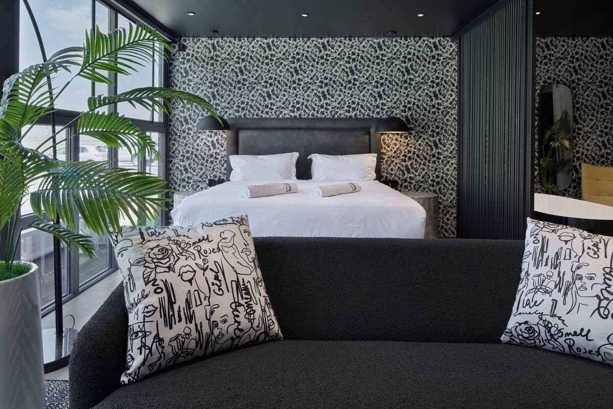 A modern bedroom with a large bed, a dark sofa, and a large window.