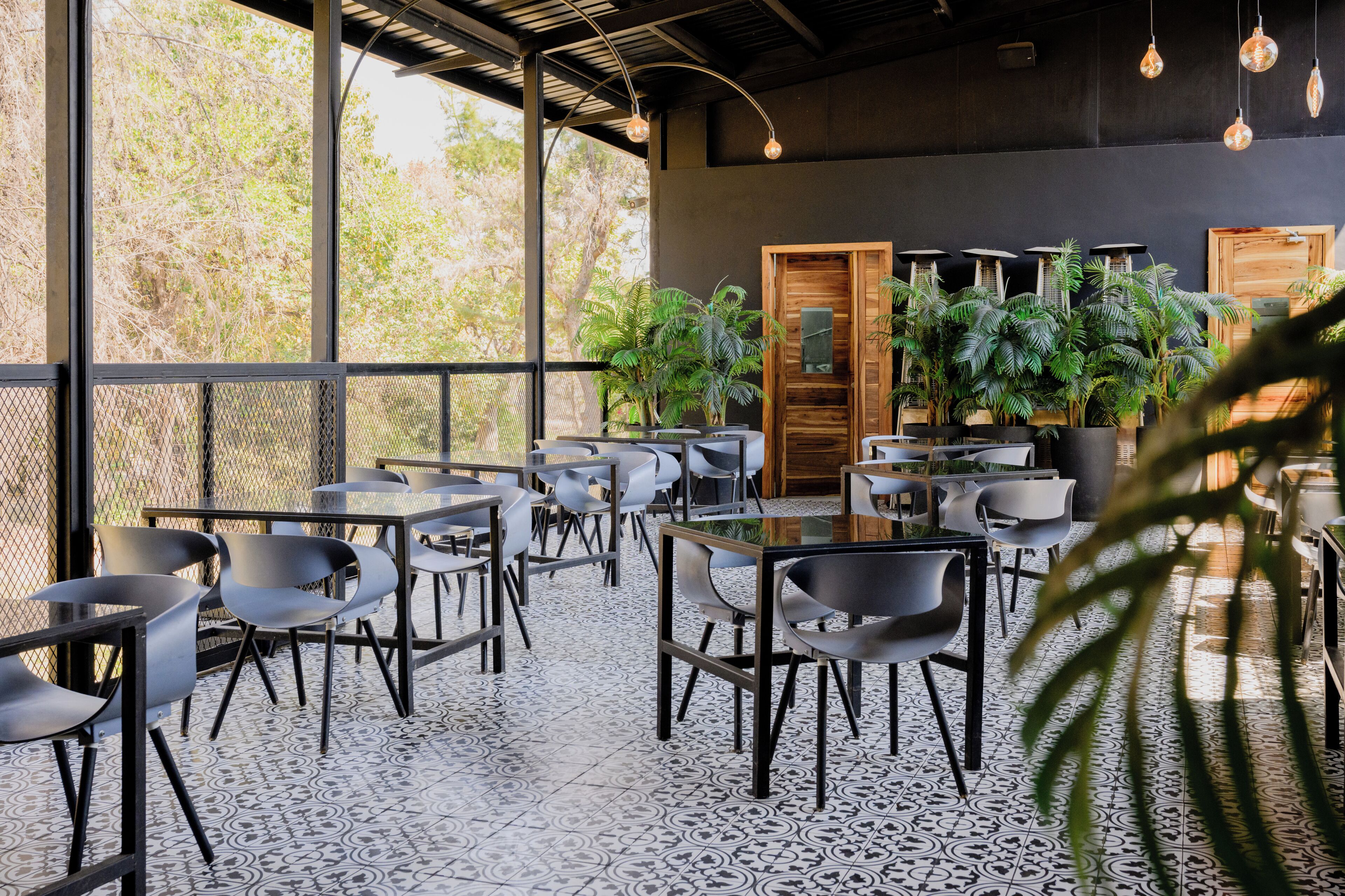 An indoor seating area with tables and chairs, large windows, and potted plants.