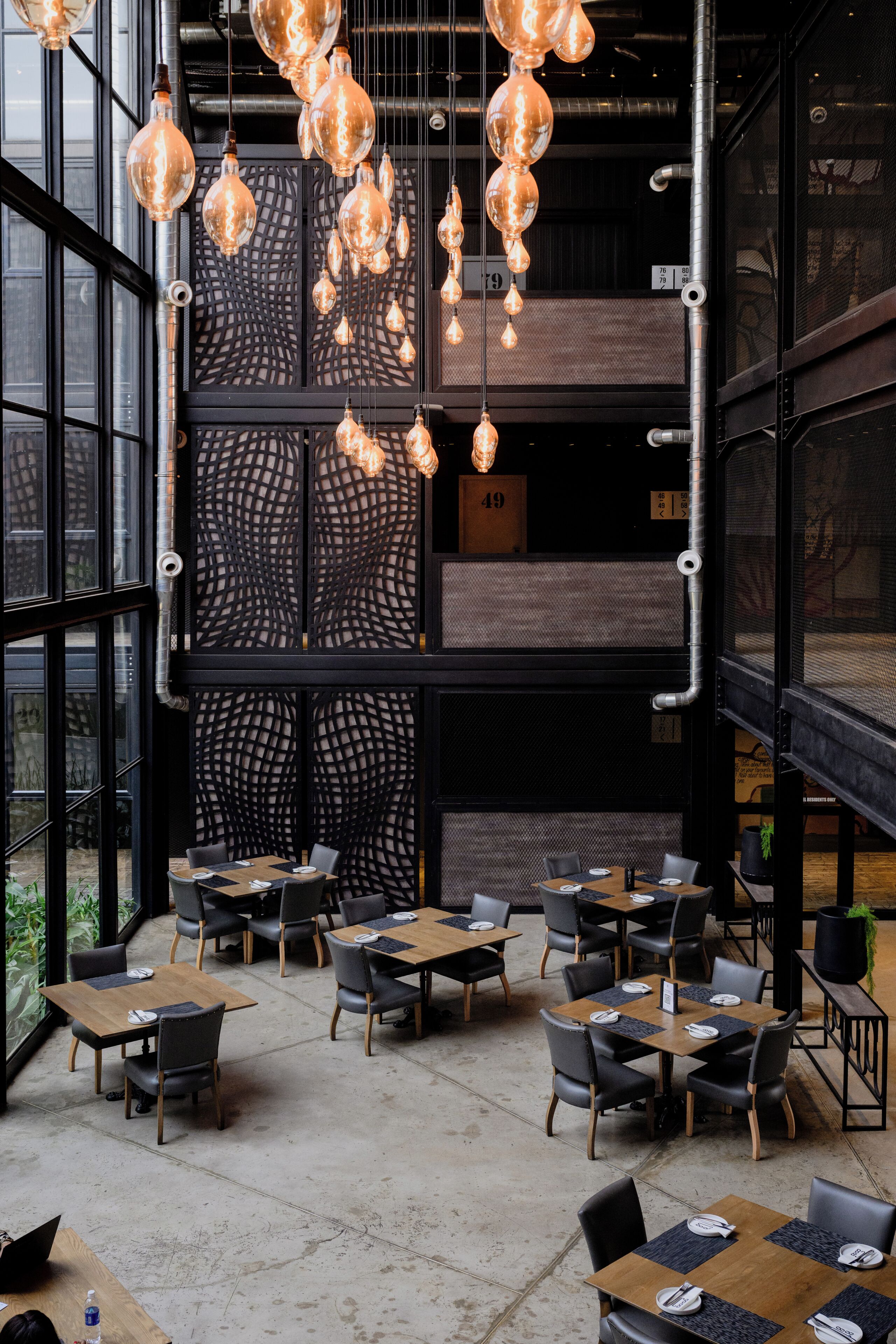 Un interior moderno con lámparas colgantes, una mezcla de muebles de madera y metal, y ventanas amplias que ofrecen vistas.