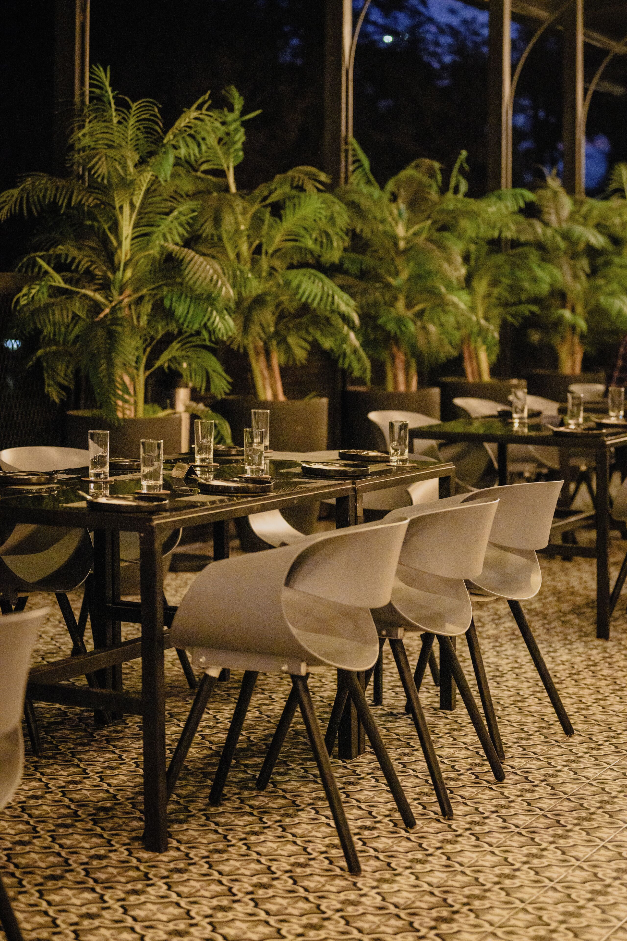 A restaurant with tables set for dining, chairs, and potted plants.
