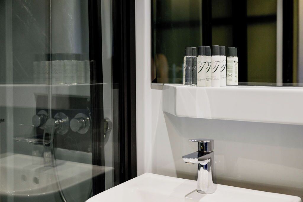 A bathroom with a glass shower enclosure, a white sink, and a shelf with toiletries.