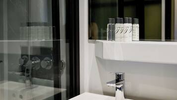 A bathroom with a glass shower enclosure, a white sink, and a shelf with toiletries.