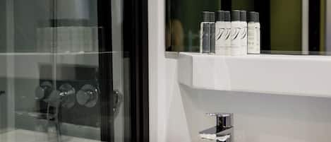 A bathroom with a glass shower enclosure, a white sink, and a shelf with toiletries.