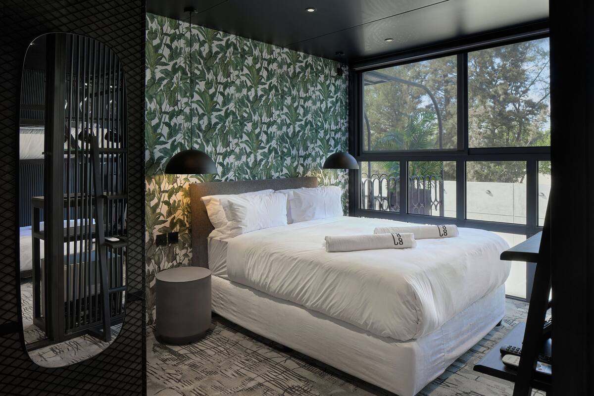A modern hotel room with a large bed, a window with a view, a patterned wall, and a unique black partition.
