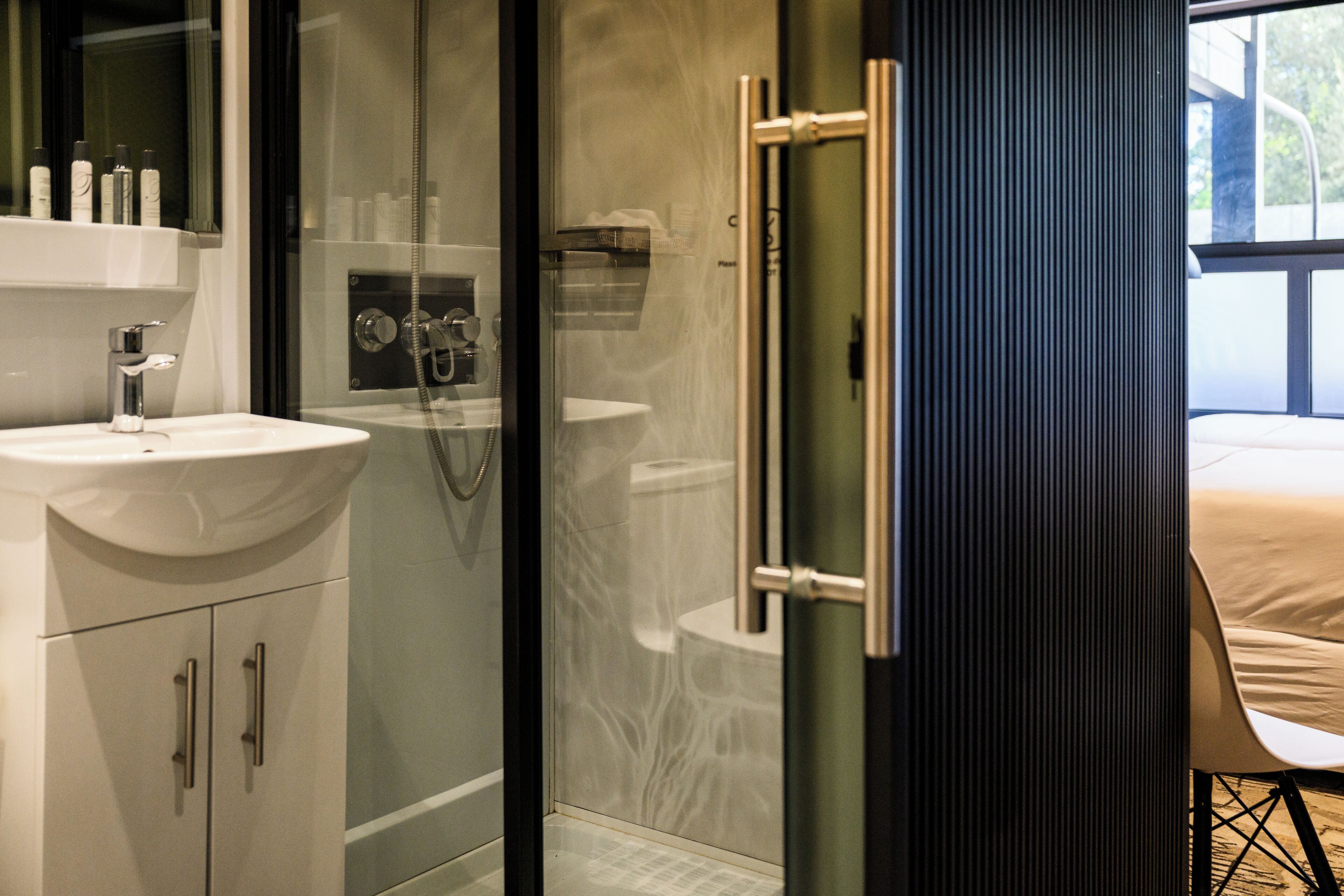 Un baño moderno con ducha acristalada, lavamanos blanco y váter a la vista.
