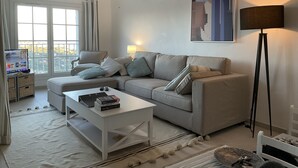 A modern living room with a sofa, coffee table, and floor lamp. There is a TV on a stand and a window with curtains. - Xxxxxxxxxx (Sainte-Maxime)
