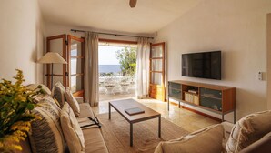 Ein Wohnzimmer mit Sofa, Couchtisch, Fernseher und Meerblick durch offene Türen.