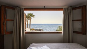 Ein Schlafzimmer mit großem Fenster und Blick auf das Meer, einem Bett und Vorhängen.