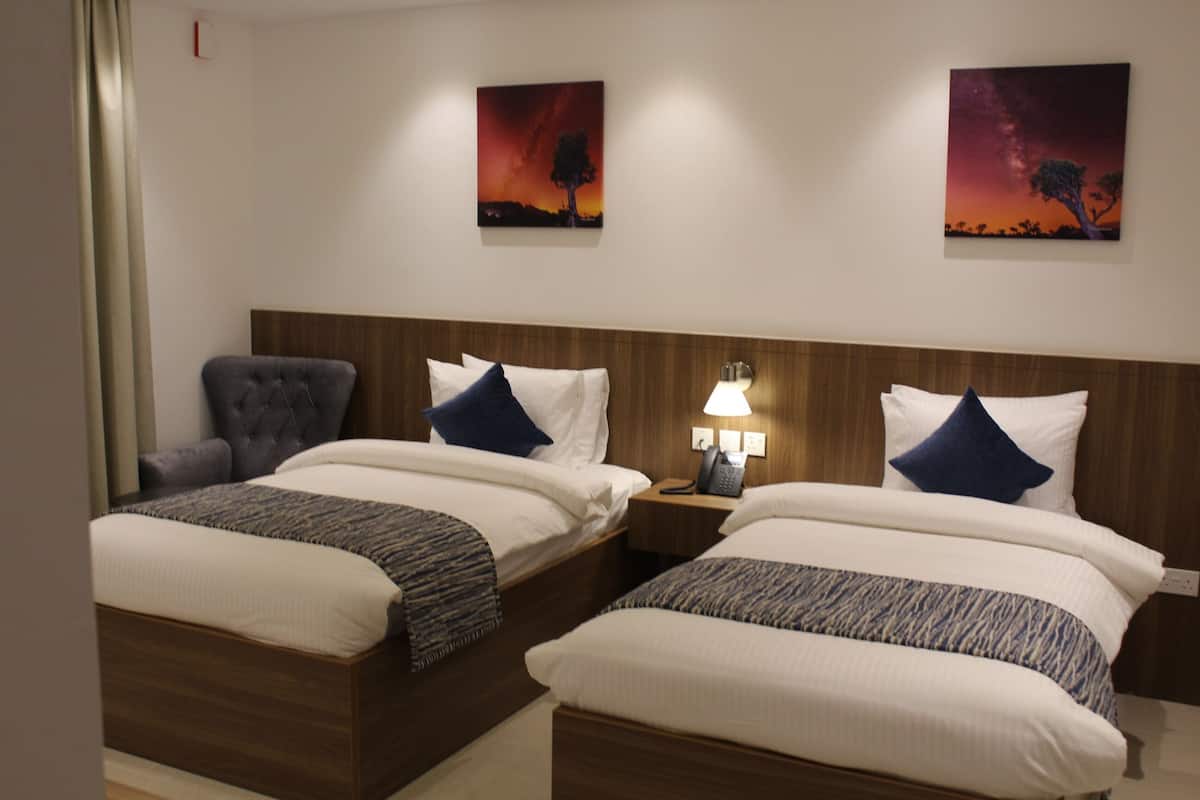 A hotel room with two beds, a nightstand with a lamp, and two paintings on the wall.