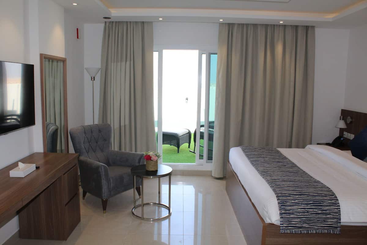 A hotel room with a bed, a desk, a chair, a small table with a basket, and a balcony with a view.