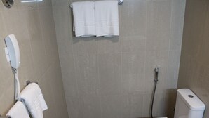 A small, modern bathroom with a toilet, a shower, and a hand dryer. - DUQM EXPRESS (Duqm)