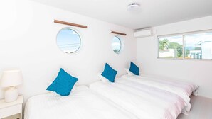 A bedroom with two beds, a bedside table with a lamp, and two round windows.