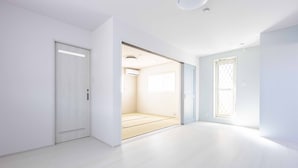 A spacious, modern room with a sliding door leading to a bathroom, a large window providing natural light, and a clean, minimalist design.