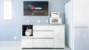 A modern kitchen with a flat-screen TV mounted above a marble countertop, a microwave, and a refrigerator.
