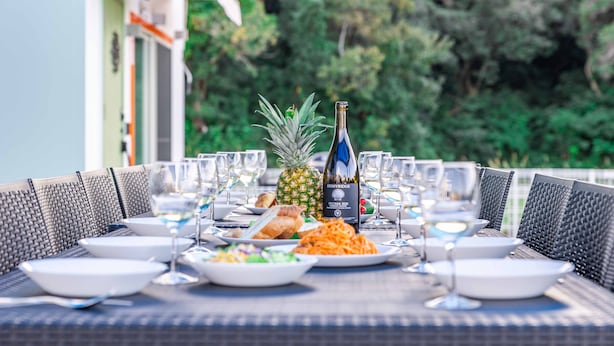 A table set for a meal with plates, glasses, and a bottle of wine, surrounded by wicker chairs.