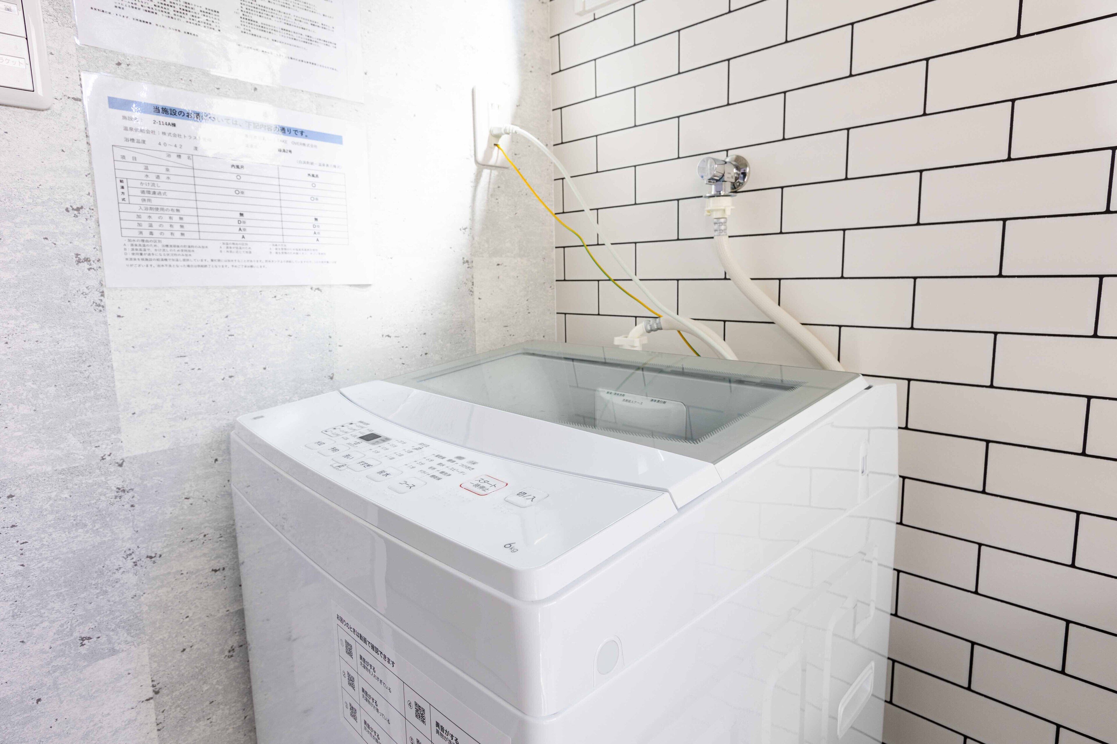 A front-loading washing machine in a laundry room with a tiled wall and a paper on the wall.