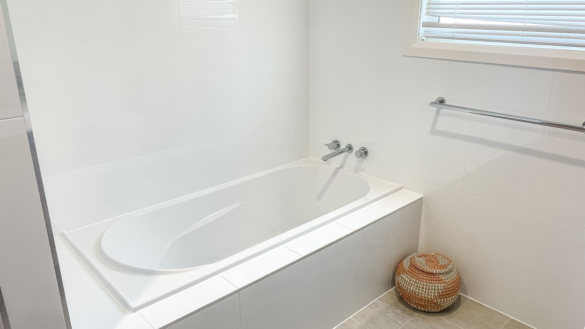 A modern bathroom with a white bathtub, a small woven stool, and a towel rack.