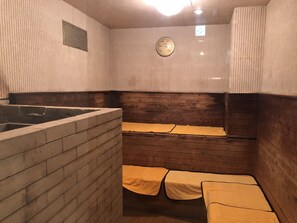 Een kleine, zwak verlichte kamer met een houten bank en een bakstenen muur.