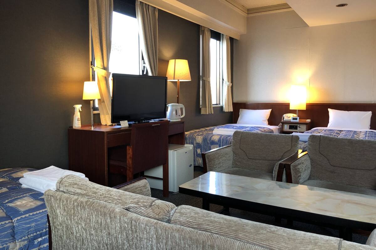 Habitación de hotel con dos camas, un escritorio, televisión, cafetera y dos lámparas.