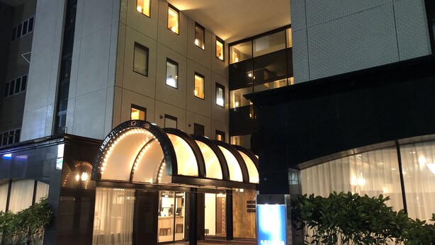 A hotel entrance with a modern design, featuring a curved glass facade and illuminated signage. - Hotel 28 Hiroshima (Hiroshima)