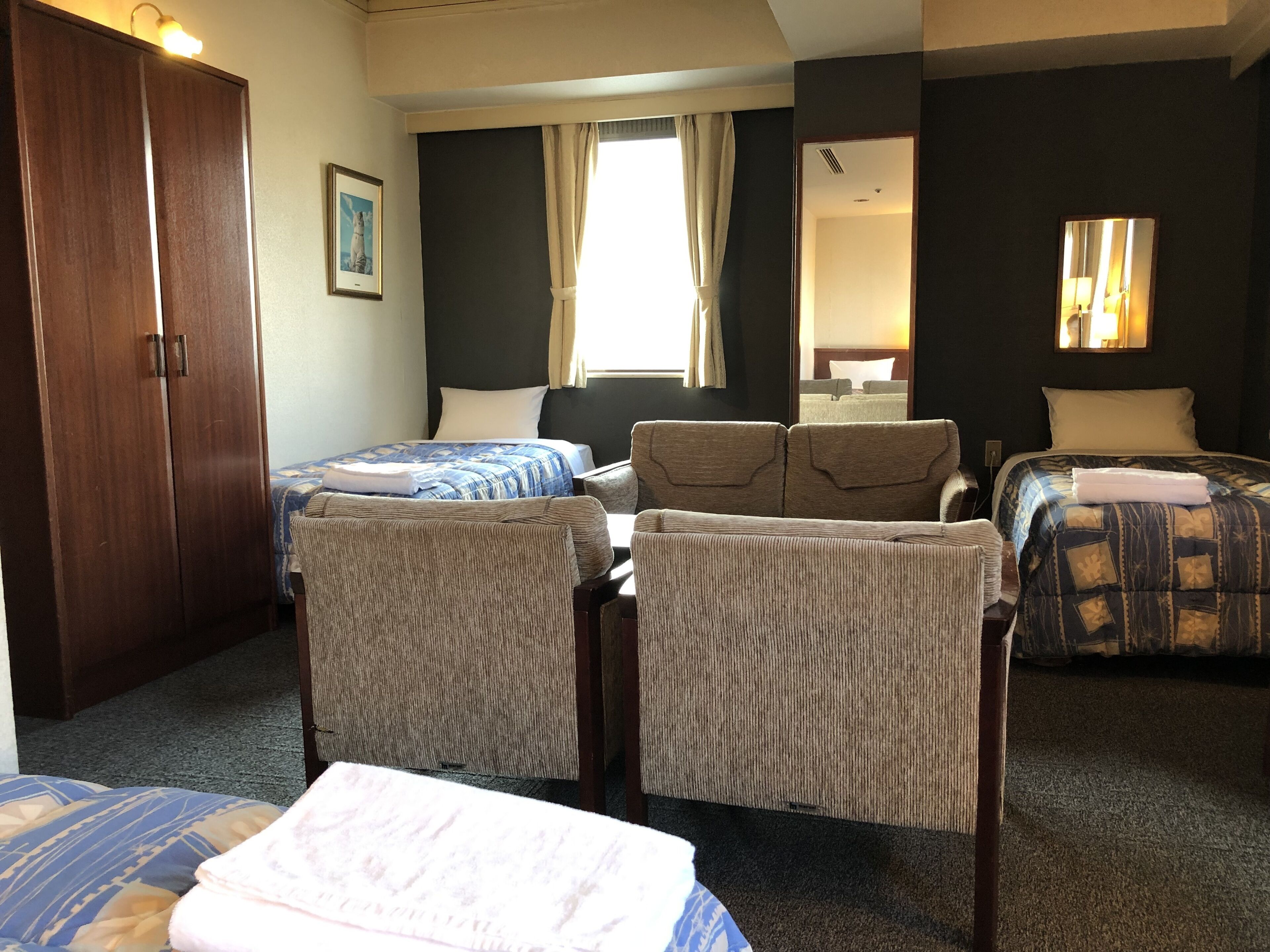 Una habitación de hotel con dos camas individuales, un sofá, un escritorio y un armario.