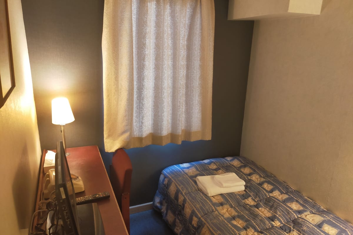 Una habitación de hotel con cama, escritorio, lámpara y ventana con cortinas.