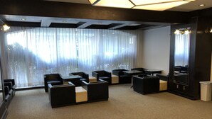 A modern hotel room with a seating area featuring black sofas and tables, large windows with sheer curtains, and a geometric ceiling design. - Hotel 28 Hiroshima (Hiroshima)