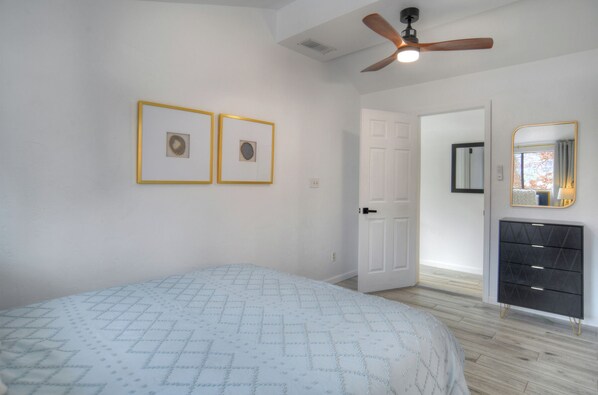 A bedroom with a bed, a dresser, a ceiling fan, and two framed pictures on the wall.
