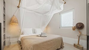 A bedroom with a canopy bed, a bedside table, a lamp, and a decorative plant.