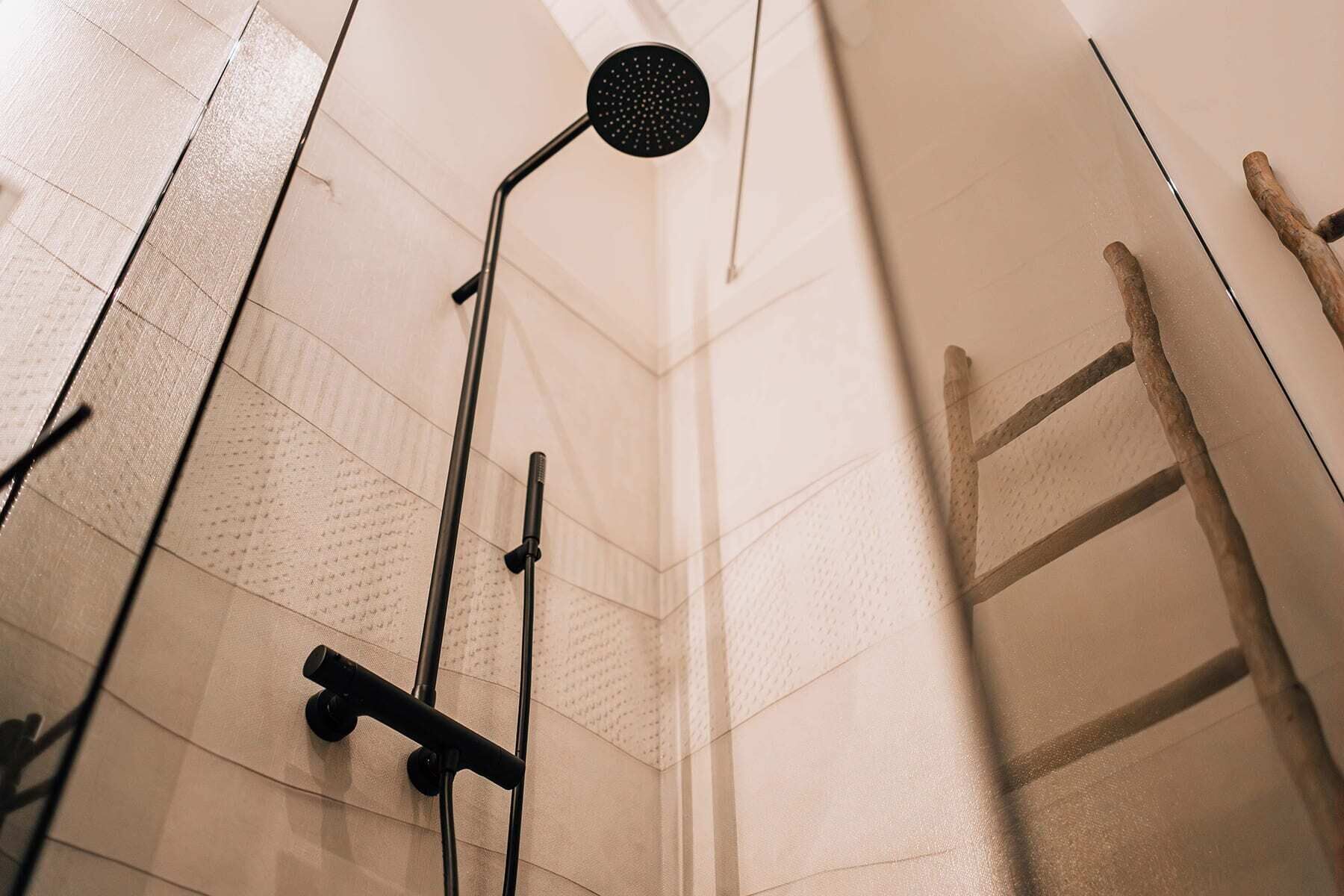 A shower area with a handheld showerhead, a wall-mounted showerhead, and a wooden ladder.