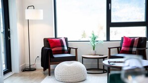 Een moderne woonkamer met twee fauteuils, een rond hock, een bijzettafeltje, een vloerlamp en een potplant.