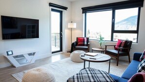 Een moderne woonkamer met een flatscreentelevisie, een bank, een salontafel en een groot raam met uitzicht.