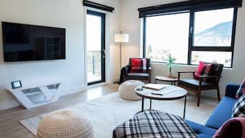 Una sala de estar moderna con un televisor de pantalla plana, un sofá, una mesa de centro y un ventanal con vistas.