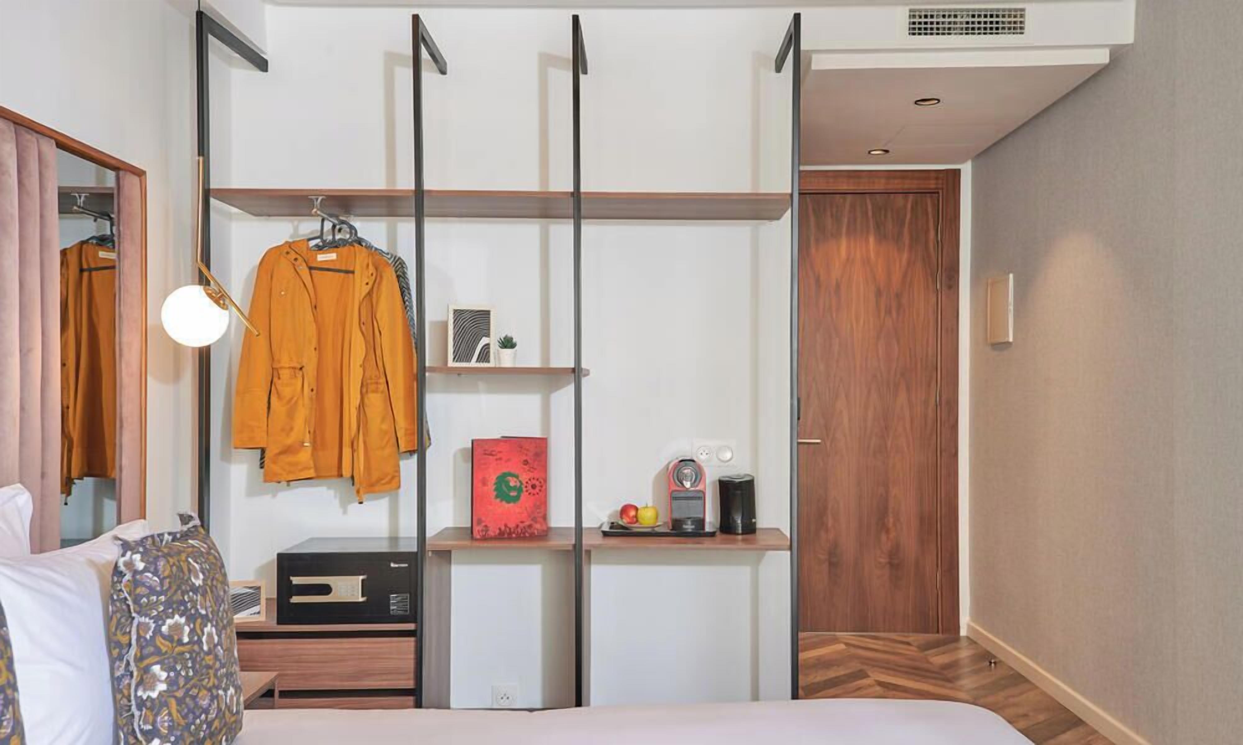 A bedroom with a bed, a bedside table with a radio, a wardrobe with a mirror, and a door.