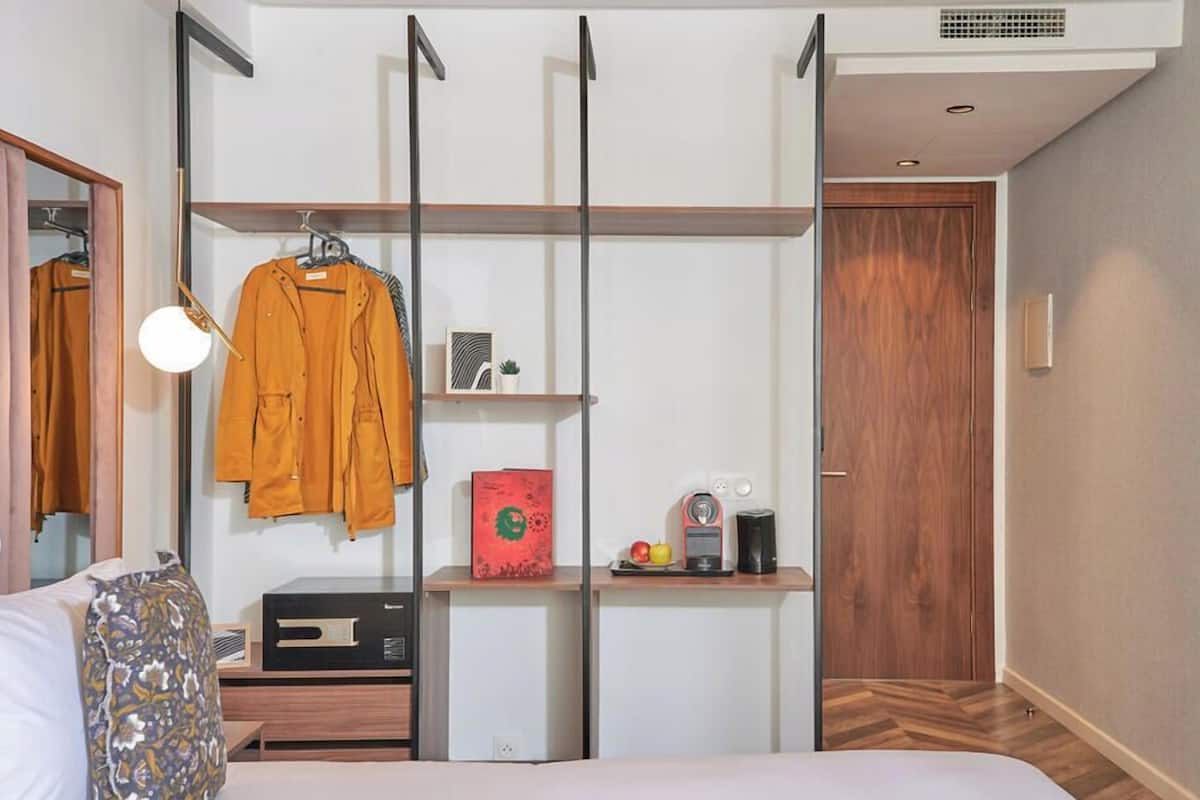 A bedroom with a bed, a bedside table with a radio, a wardrobe with a mirror, and a door.