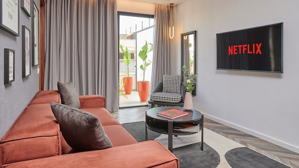 A modern living room with a sofa, a chair, a coffee table, and a TV displaying "NETFLIX". - StayHere Rabat - Agdal Boutique Hotel (Rabat)