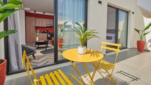 A modern outdoor seating area with a yellow table and chairs, a potted plant, and a sliding glass door leading to a kitchen and living space. - StayHere Rabat - Agdal Boutique Hotel (Rabat)