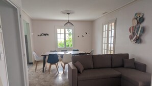 Un saló modern amb un sofà seccional marró, una taula de dinar amb caires i una finestra gran amb vista a vegetació.