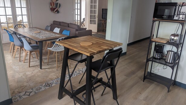 Àmplia zona d'estar amb una taula de dinar de fusta, cadires modernes, un sofà i una cuina equipada.