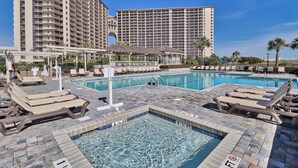 A hotel pool area with lounge chairs, a small gazebo, and a large building in the background. - Recently Renovated Oceanfront Condo, Private Resort +Free Attraction Tickets! (Myrtle Beach)